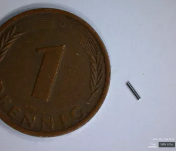 Sehr kleines Edelstahlröhrchen neben einer 1-Pfennig-Münze zum Größenvergleich; das Rohr wirkt extrem fein und kurz.
