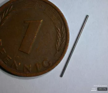 Ein langes, dünnes Edelstahl-Feinrohr neben einer 1-Pfennig-Münze als Maßstab, auf hellem Hintergrund platziert.